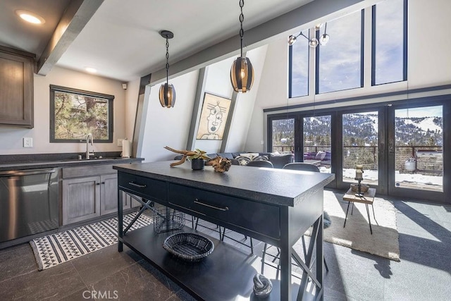 kitchen with a sink, stainless steel dishwasher, beam ceiling, dark countertops, and decorative light fixtures