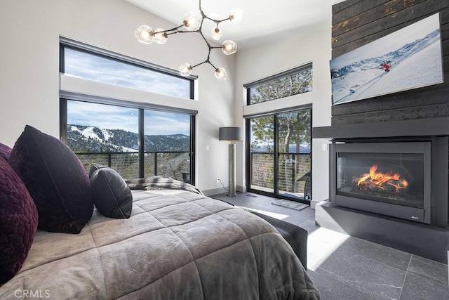 bedroom with baseboards, a glass covered fireplace, a towering ceiling, access to exterior, and a chandelier