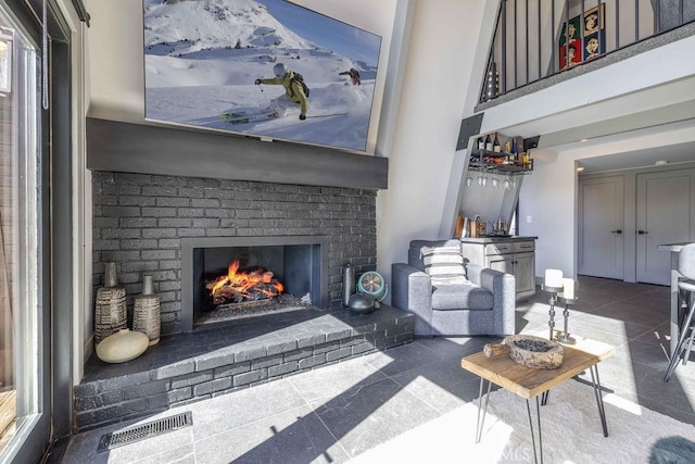 tiled living area with a high ceiling, visible vents, baseboards, a brick fireplace, and a dry bar