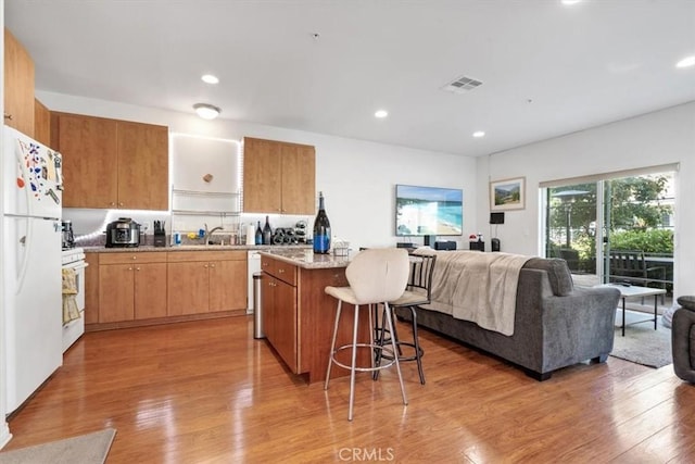 kitchen with white appliances, light wood finished floors, visible vents, a kitchen island, and open floor plan