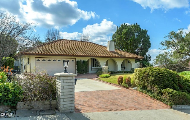 mediterranean / spanish house featuring an attached garage, a tiled roof, decorative driveway, stucco siding, and a chimney