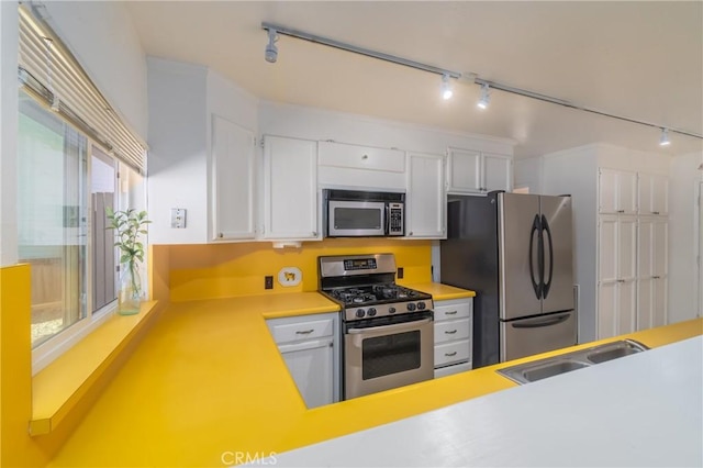 kitchen with stainless steel appliances, a sink, white cabinets, light countertops, and rail lighting