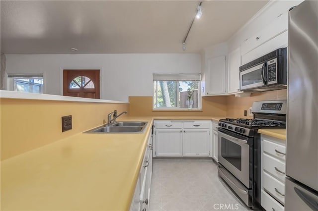 kitchen featuring stainless steel appliances, light countertops, white cabinets, a sink, and track lighting