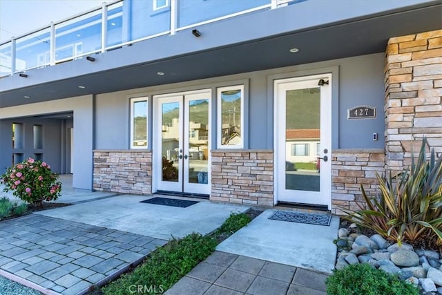 entrance to property with stone siding, french doors, and stucco siding
