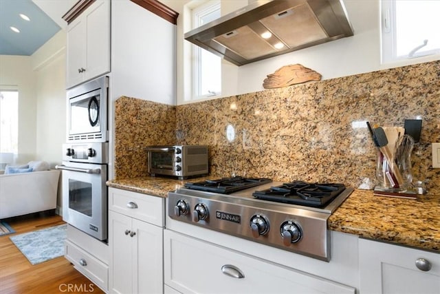 kitchen featuring a toaster, decorative backsplash, white cabinets, wall chimney exhaust hood, and appliances with stainless steel finishes