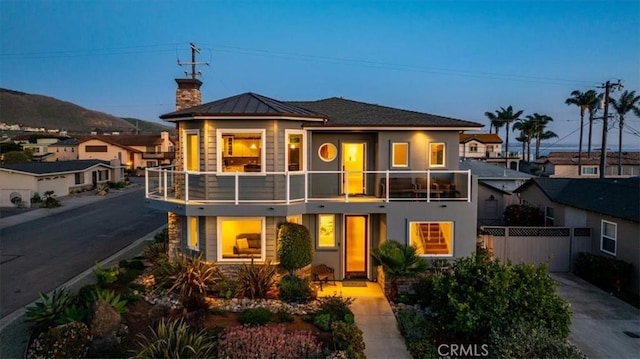view of front of home with metal roof, a balcony, fence, driveway, and a standing seam roof