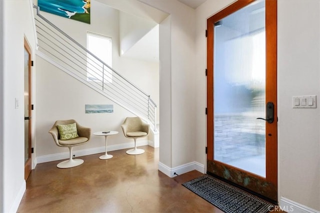 entryway with finished concrete floors, stairway, and baseboards