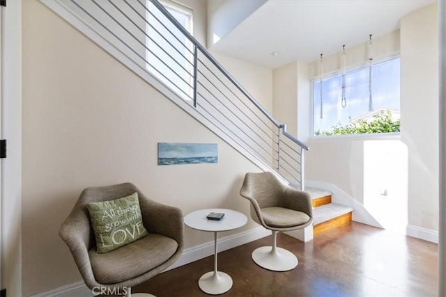 living area with finished concrete flooring, stairway, and baseboards