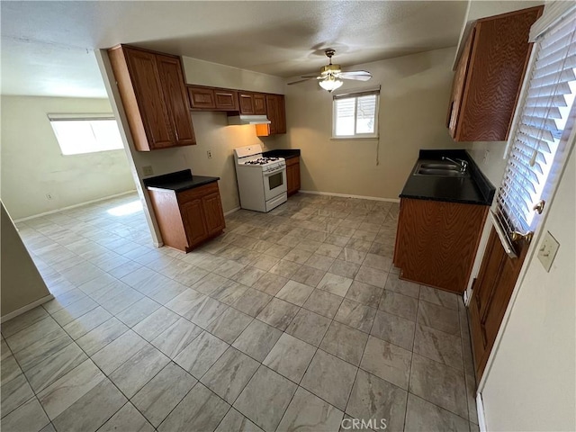 kitchen with dark countertops, under cabinet range hood, white gas range oven, and a sink