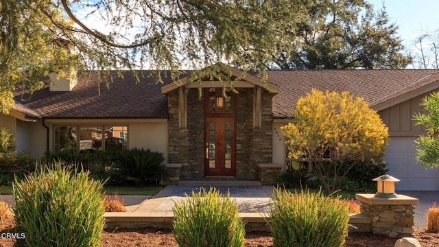 view of front of property featuring a chimney, stucco siding, a shingled roof, board and batten siding, and stone siding