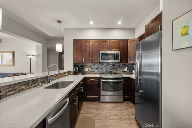 kitchen with tasteful backsplash, appliances with stainless steel finishes, light stone counters, decorative light fixtures, and a sink