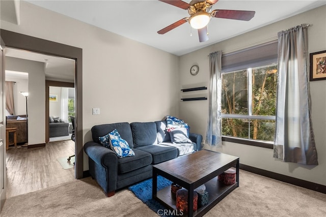 living room featuring light carpet, baseboards, and a ceiling fan