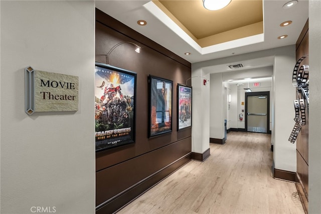 corridor featuring light wood-style flooring, recessed lighting, visible vents, baseboards, and a tray ceiling