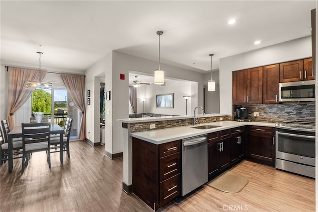 kitchen featuring decorative light fixtures, a peninsula, stainless steel appliances, light countertops, and a sink