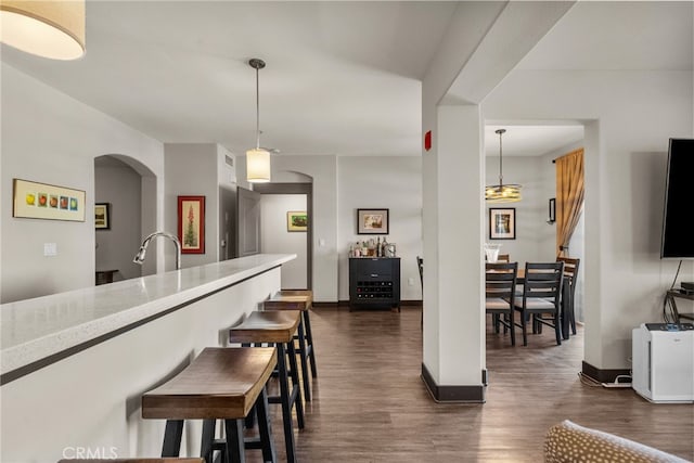 kitchen featuring baseboards, arched walkways, dark wood-type flooring, and decorative light fixtures