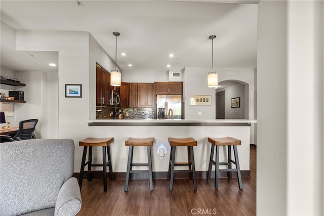 kitchen featuring tasteful backsplash, dark wood-style floors, appliances with stainless steel finishes, hanging light fixtures, and a peninsula