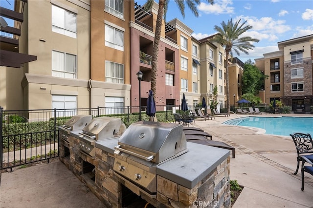 community pool featuring area for grilling, fence, an outdoor kitchen, and a patio