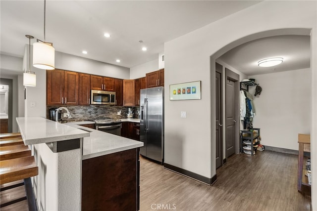 kitchen featuring a breakfast bar area, stainless steel appliances, a peninsula, decorative backsplash, and pendant lighting