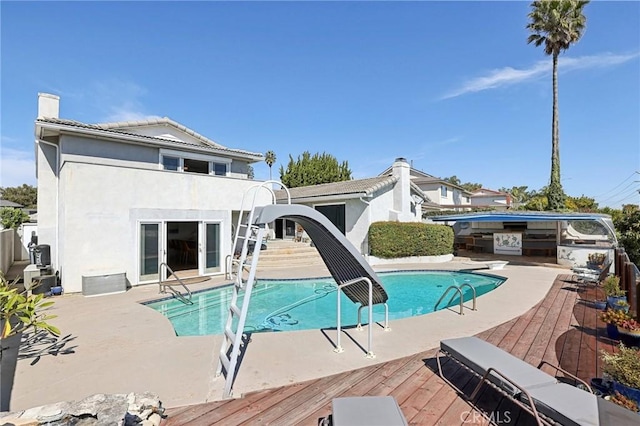 rear view of house with a deck, a chimney, an outdoor pool, and stucco siding