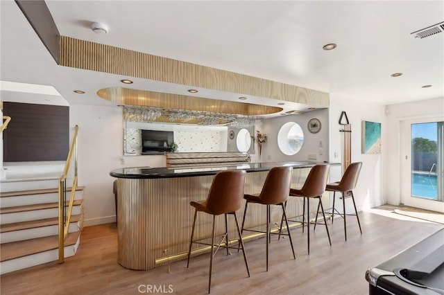 bar featuring a bar, light wood-style flooring, stairway, and visible vents