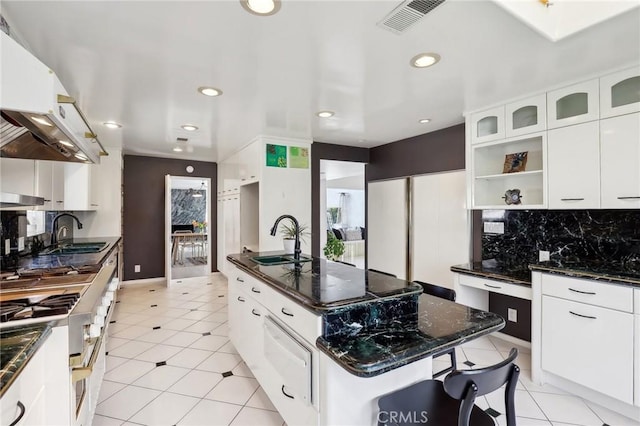 kitchen with an island with sink, white cabinetry, glass insert cabinets, and a sink