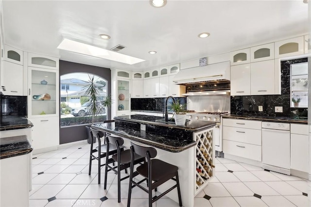 kitchen featuring white cabinets, a kitchen island with sink, glass insert cabinets, and custom range hood