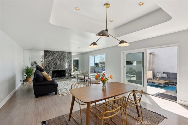 dining room featuring baseboards, a raised ceiling, a high end fireplace, wood finished floors, and recessed lighting