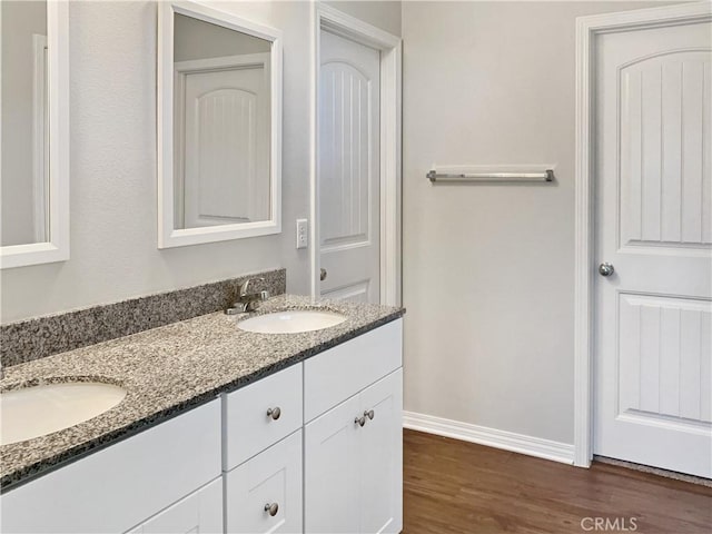 bathroom featuring double vanity, baseboards, a sink, and wood finished floors