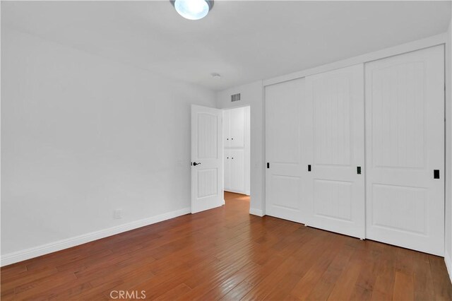 unfurnished bedroom with hardwood / wood-style flooring, baseboards, visible vents, and a closet