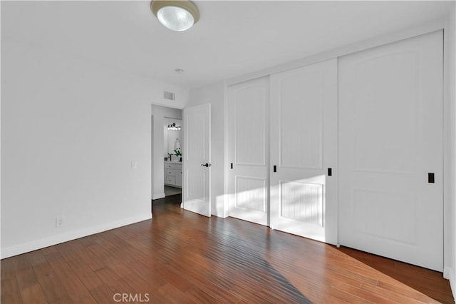 unfurnished bedroom featuring dark wood-type flooring, a closet, visible vents, and baseboards