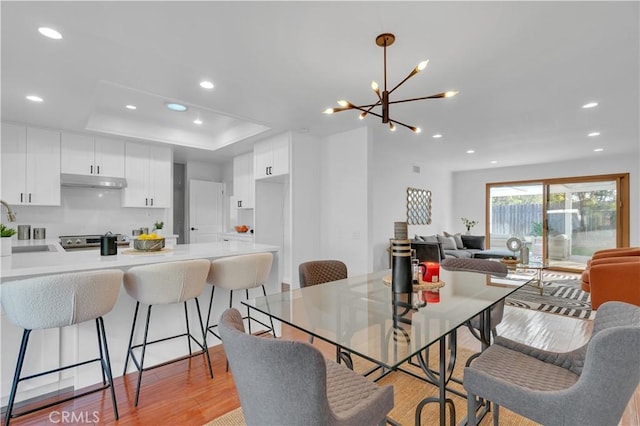 dining room with light wood-style floors, recessed lighting, a chandelier, and a raised ceiling