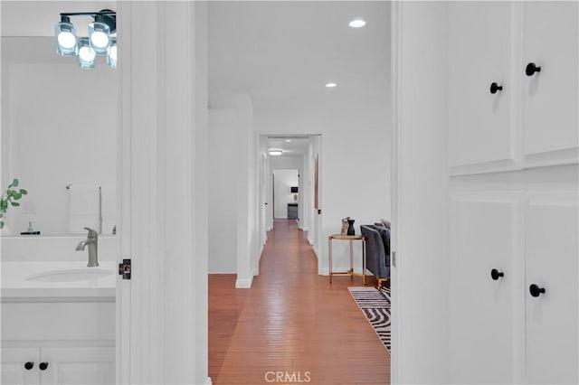 corridor featuring light wood-type flooring, baseboards, a sink, and recessed lighting