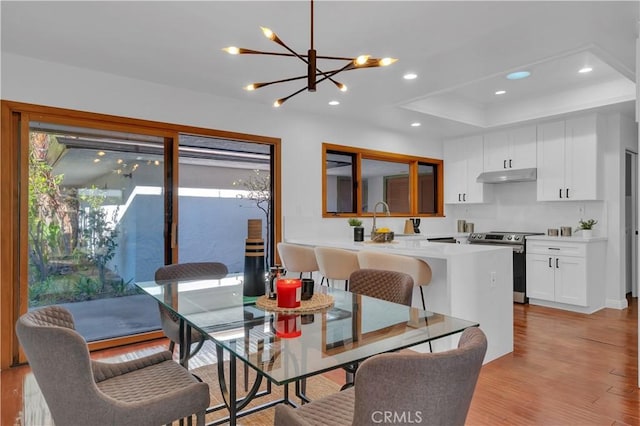 dining room featuring light wood finished floors, a tray ceiling, an inviting chandelier, and recessed lighting