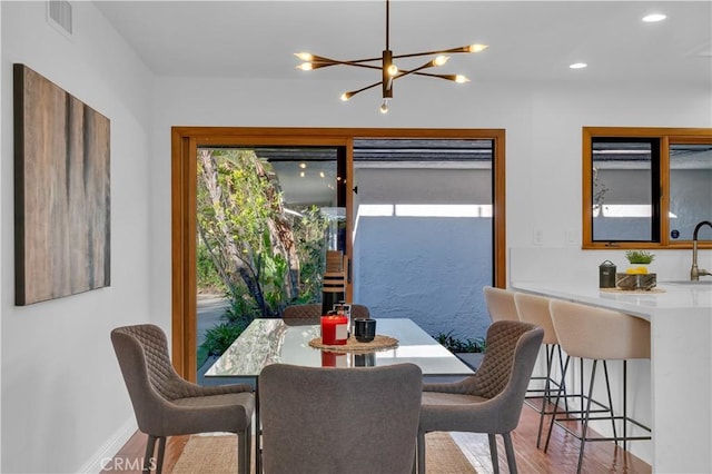 dining room with light wood finished floors, baseboards, visible vents, and a notable chandelier