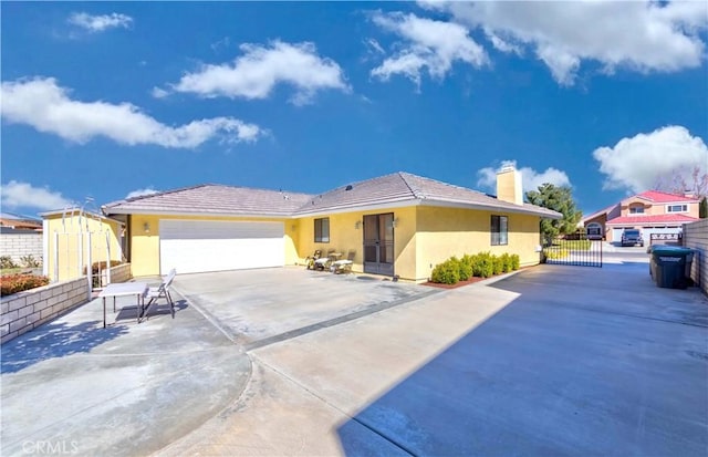 ranch-style home with driveway, a garage, a chimney, fence, and stucco siding