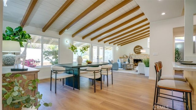 dining area featuring baseboards, lofted ceiling with beams, french doors, light wood-style floors, and a fireplace