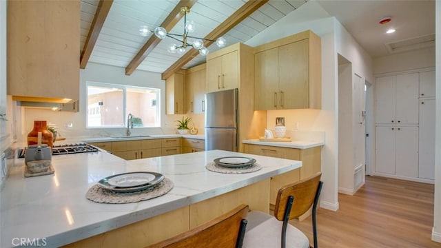 kitchen with light brown cabinets, a peninsula, a sink, freestanding refrigerator, and pendant lighting