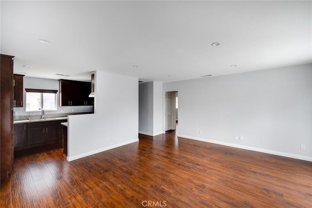 unfurnished living room with dark wood-style floors, recessed lighting, a sink, and baseboards