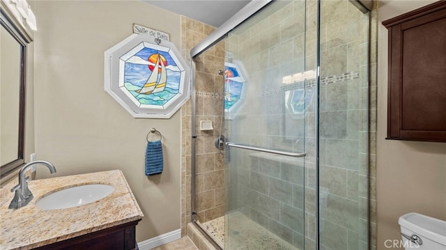 bathroom featuring baseboards, a shower stall, toilet, and vanity