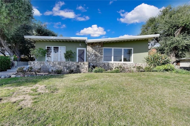 rear view of property with stucco siding, stone siding, and a yard