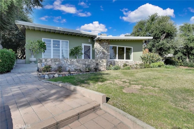 exterior space with stucco siding, stone siding, and a lawn