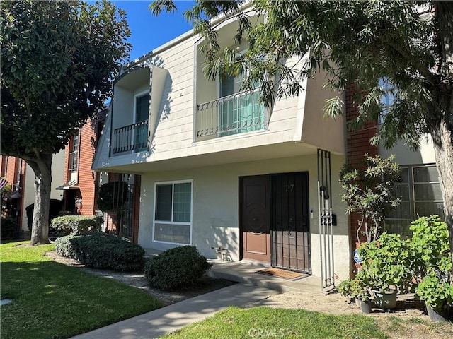 view of property with a front lawn, a balcony, and stucco siding