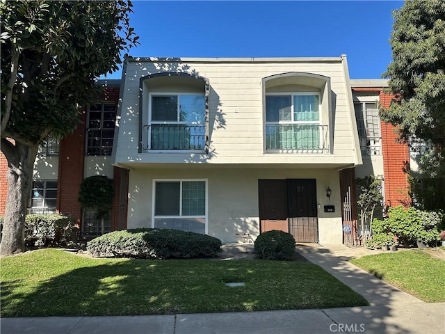 townhome / multi-family property featuring a front yard, a balcony, and stucco siding