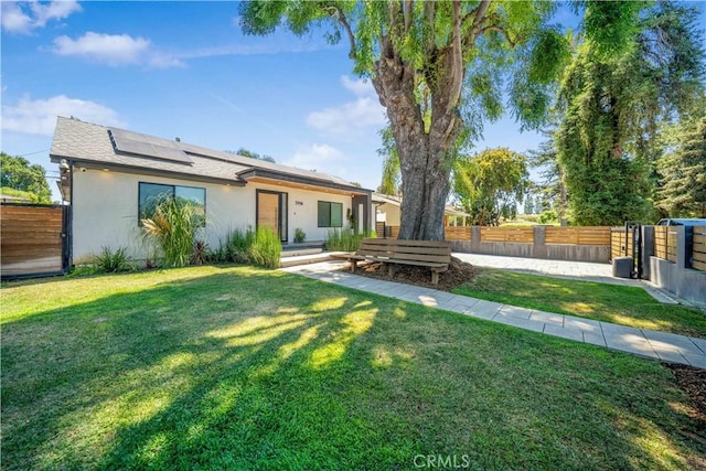 rear view of property with roof mounted solar panels, fence, a lawn, and stucco siding