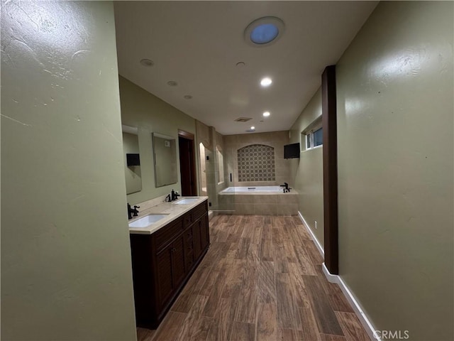 bathroom featuring a garden tub, a sink, baseboards, and wood finished floors