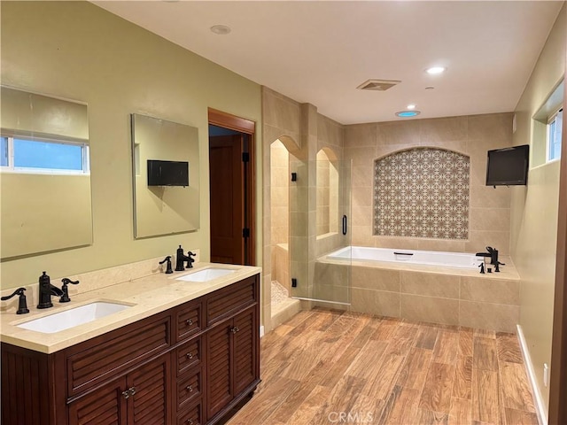 full bathroom with visible vents, wood finished floors, a sink, and tiled shower