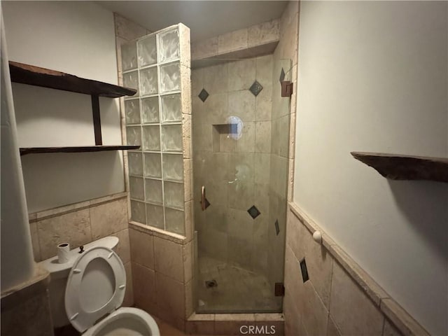 bathroom featuring toilet, a walk in shower, tile walls, and wainscoting