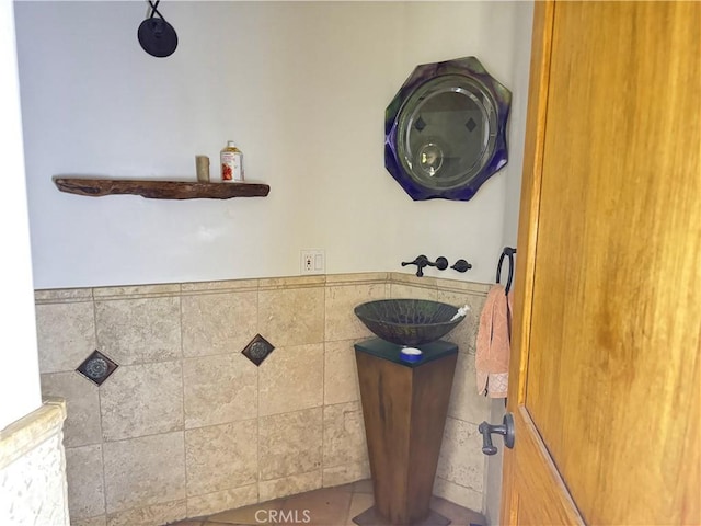 bathroom with wainscoting, a sink, and tile walls