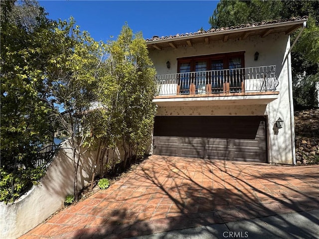 view of front facade with driveway, a garage, a balcony, a tiled roof, and stucco siding