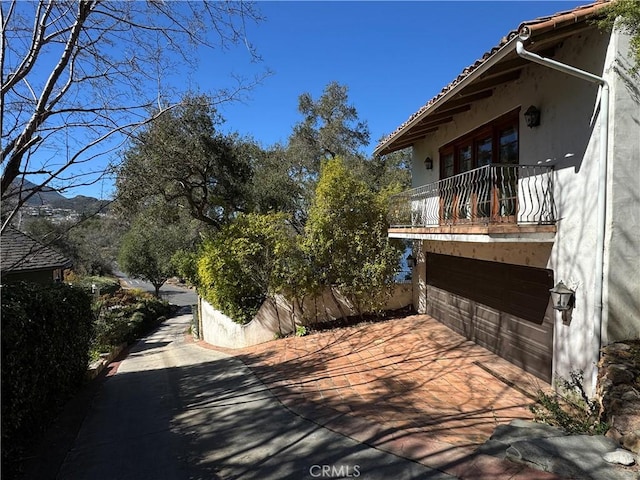 view of home's exterior with a tile roof, a balcony, an attached garage, and stucco siding